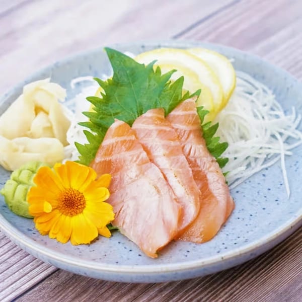 Yanagi Kitchen's salmon sashimi with ginger, wasabi, lemon, and daikon radish on a blue plate.