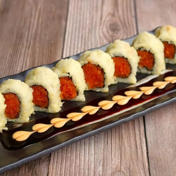 Eight pieces of deep-fried sushi with spicy tuna filling, garnished with sauce on a black plate.