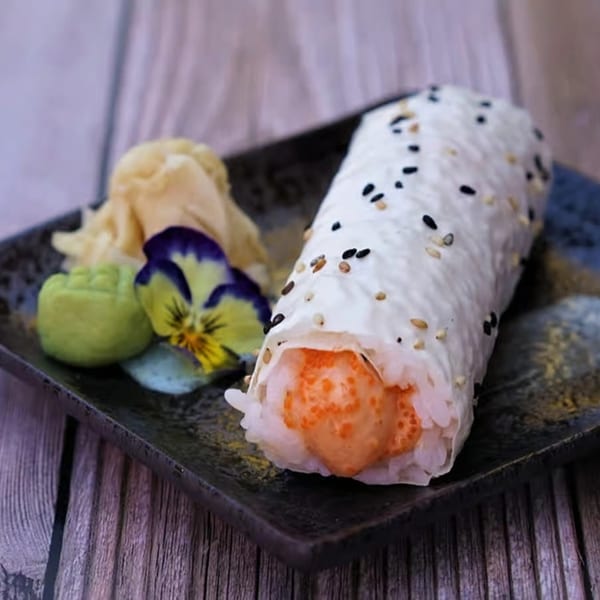Yanagi Kitchen's sushi burrito with orange roe, wasabi, ginger, and a pansy on a dark plate.