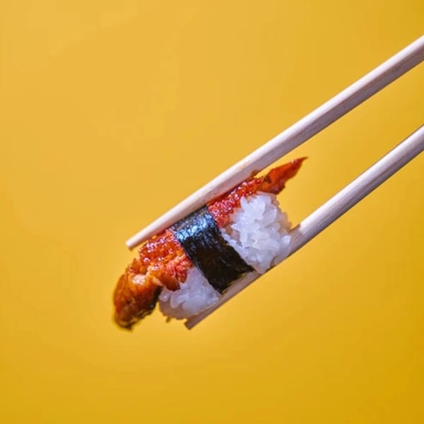 Chopsticks holding a piece of Yanagi Kitchen's eel nigiri sushi against a yellow background.