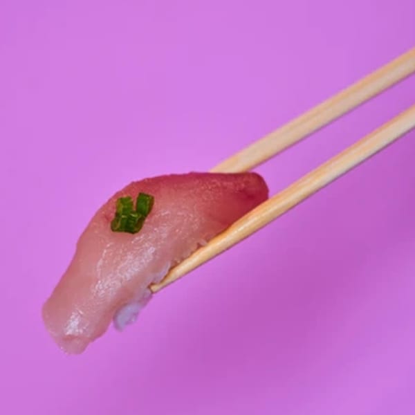 Chopsticks holding a piece of Yanagi Kitchen sushi with tuna and a green garnish.